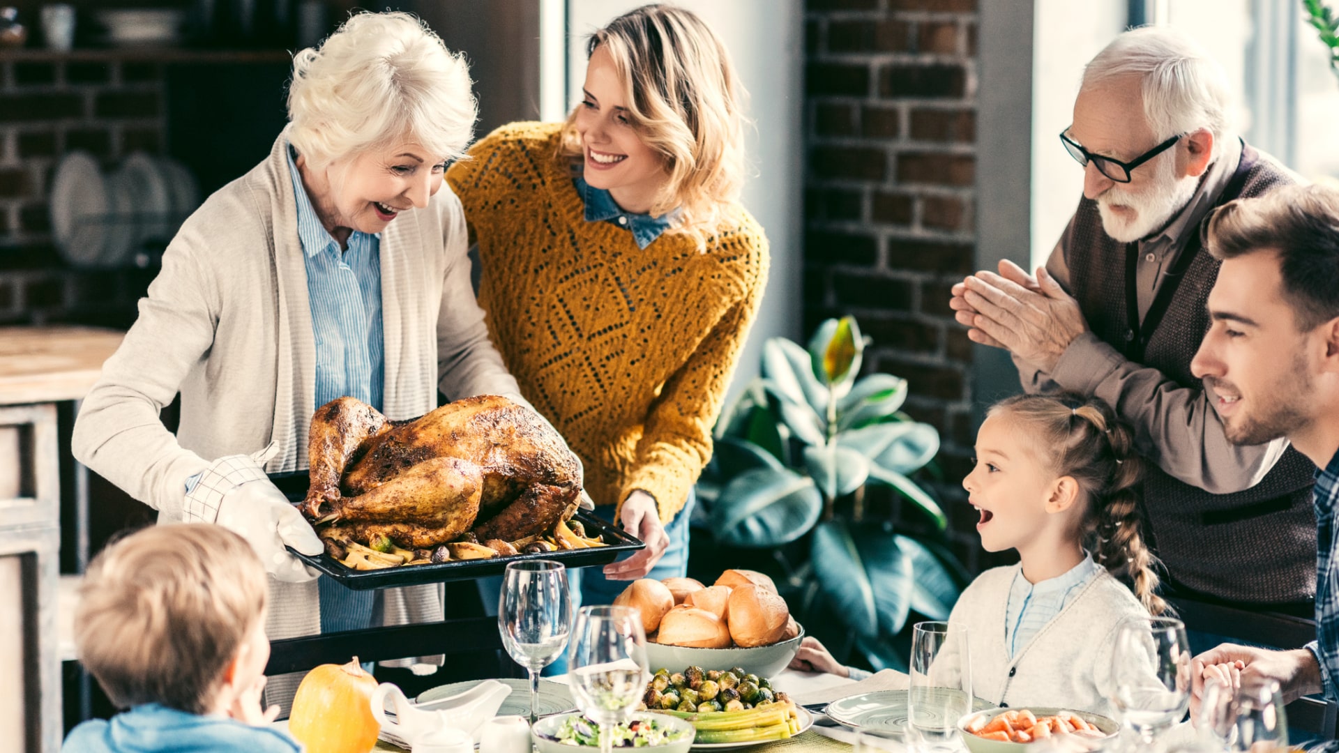 An older woman serves a roasted turkey to a family gathered around a dining table, with adults and children smiling and interacting, embodying gratitude and the warmth of Thanksgiving ideas.