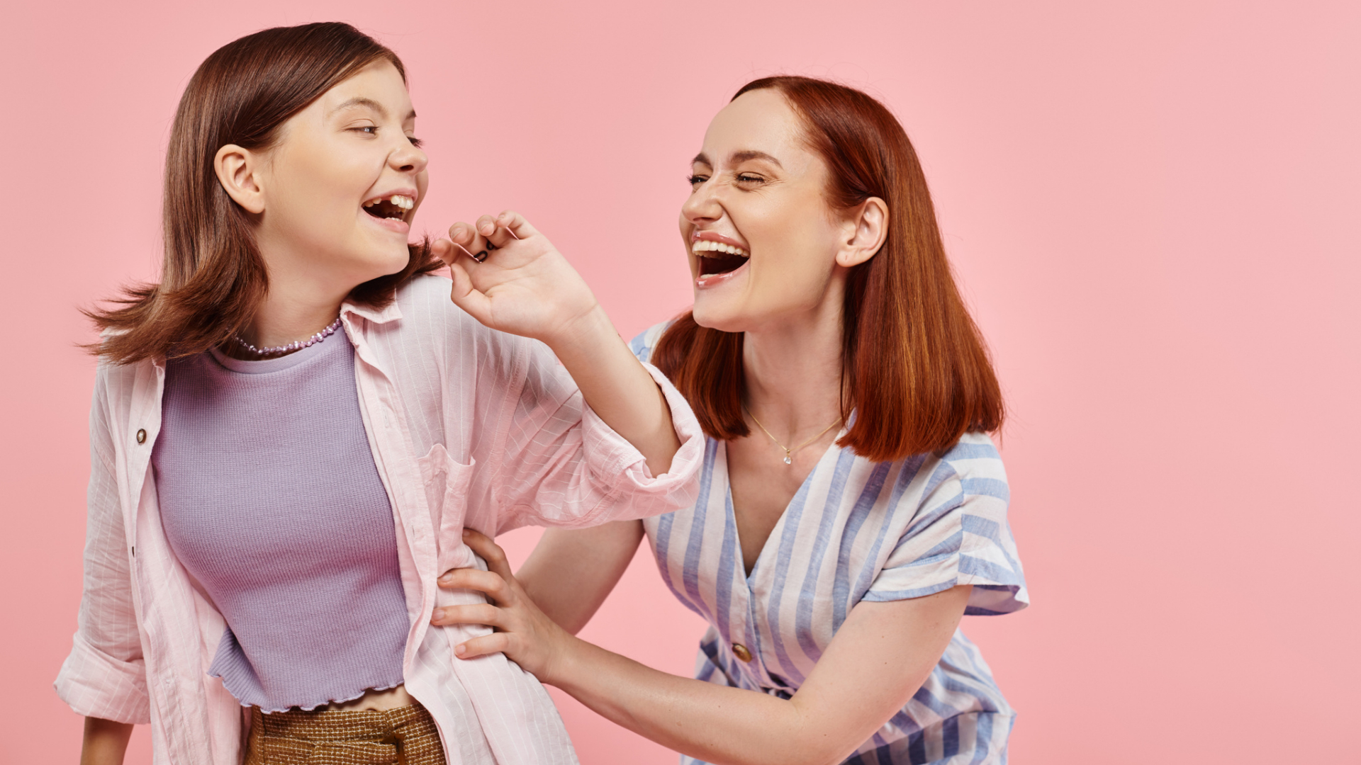 Two women, possibly mother and daughter, stand in front of a pink background laughing and smiling together, beautifully capturing the joy found in parenting and celebrating a strong child’s love language.