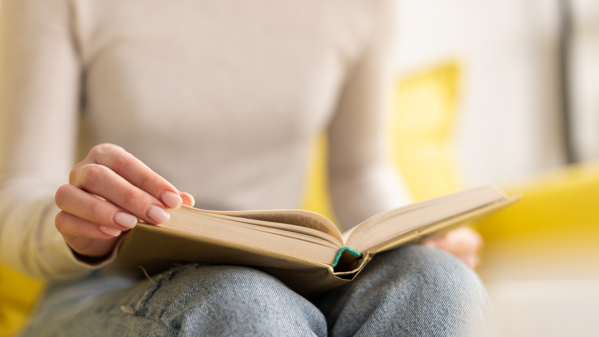 A person sits cross-legged wearing jeans and a light sweater, holding an open book—A Daughter of Fair Verona by Shakespeare—and turning a page as they begin their review.